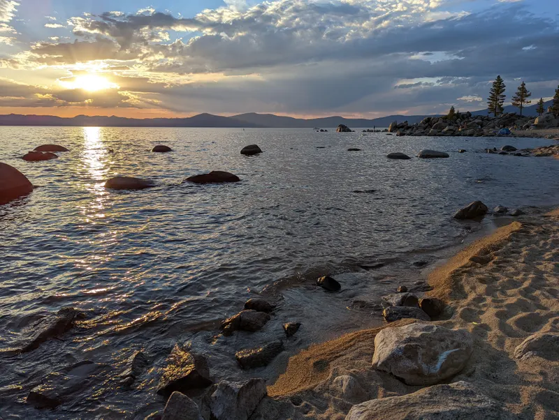 Sunset over the lake at Chimney Beach, with sand and rocks in the foreground.