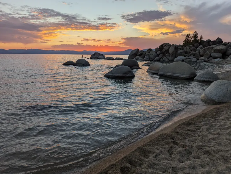 Rounded boulders in the water at Chimney Beach under an orange and pink sunset sky.
