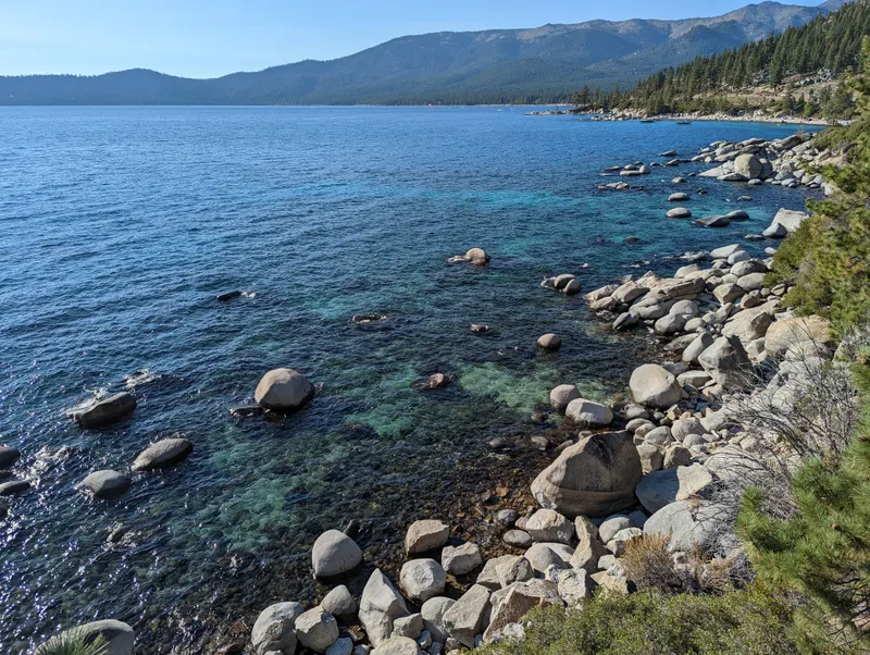 The lake from the East Shore Trail, with deep blue water, rocky shore and mountains in the distance.