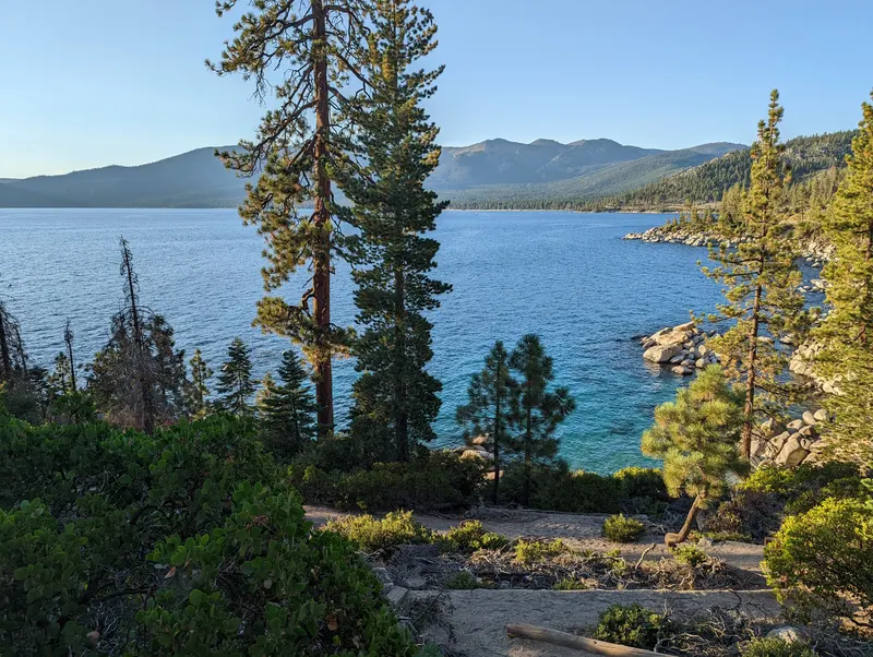 Blue water in Emerald Cove on the east shore of Lake Tahoe, seen through pines with mountains across the lake.