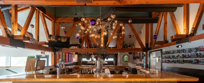 A timber-beamed room with a round chandelier over the bar.