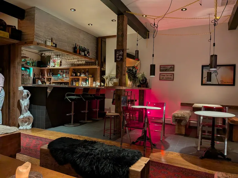 A cocktail bar with high stools and a pink-lit seating nook.
