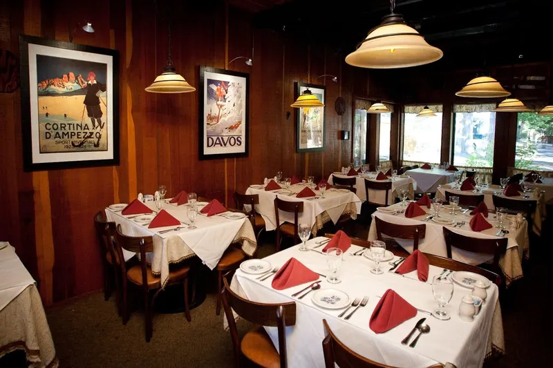 A dining room with white tablecloths, red napkins and framed ski posters on the walls.