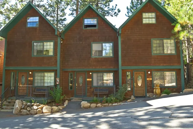 Three brown shingle lodge buildings with green trim and stone planters out front.