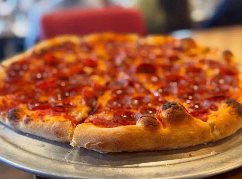 A pepperoni pizza with a charred, puffy crust on a metal tray.