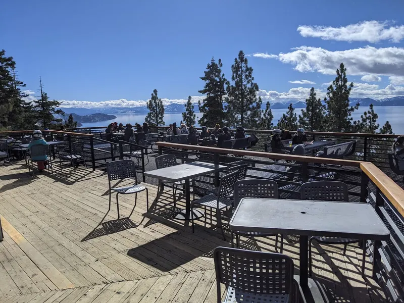 A sunny deck with tables and a wide view of Lake Tahoe through the pines.