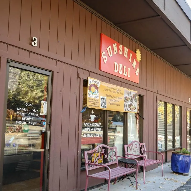 The Sunshine Deli front door with its red sign and a hours list.