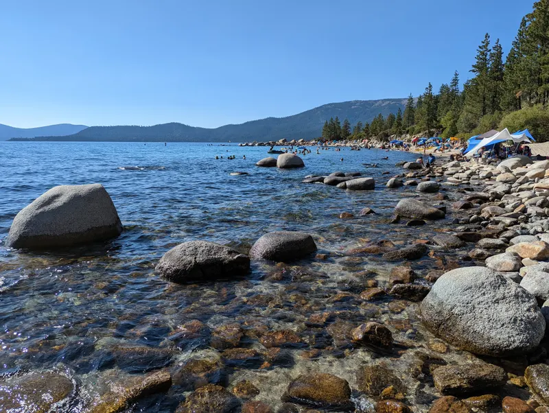 Rocky shallows at Hidden Beach with round boulders and pine trees along the shore.