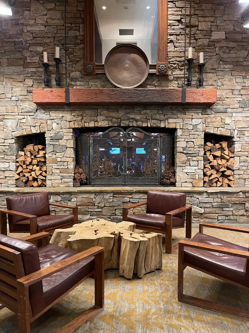 A stone fireplace with stacked logs and leather chairs around a log-slice table in a lounge at the Hyatt Regency Lake Tahoe.