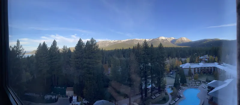 A wide window view from the Hyatt Regency Lake Tahoe over pines, the resort pool and mountains.