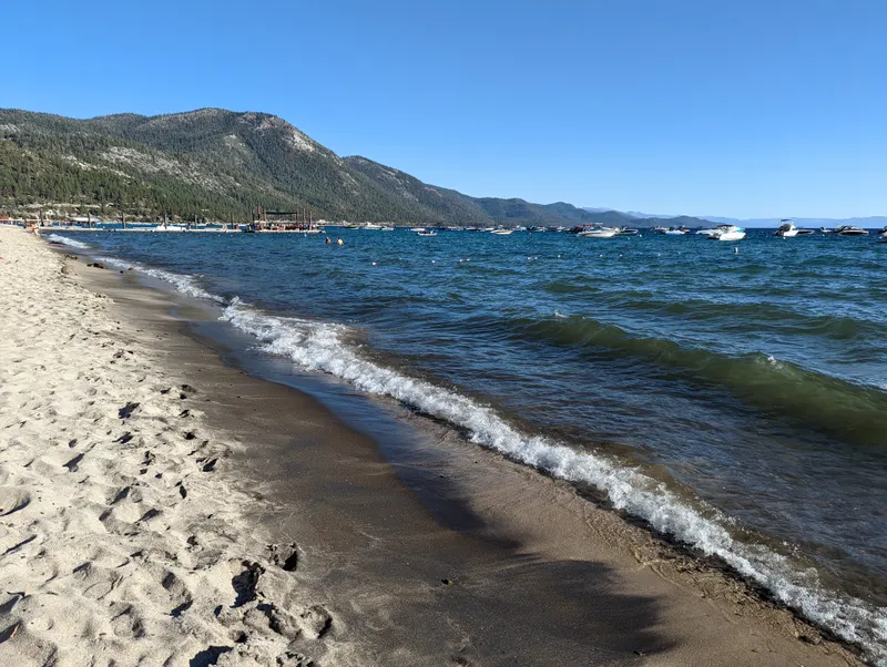 A sandy shoreline at Incline Beach with small waves rolling in and mountains behind the lake.