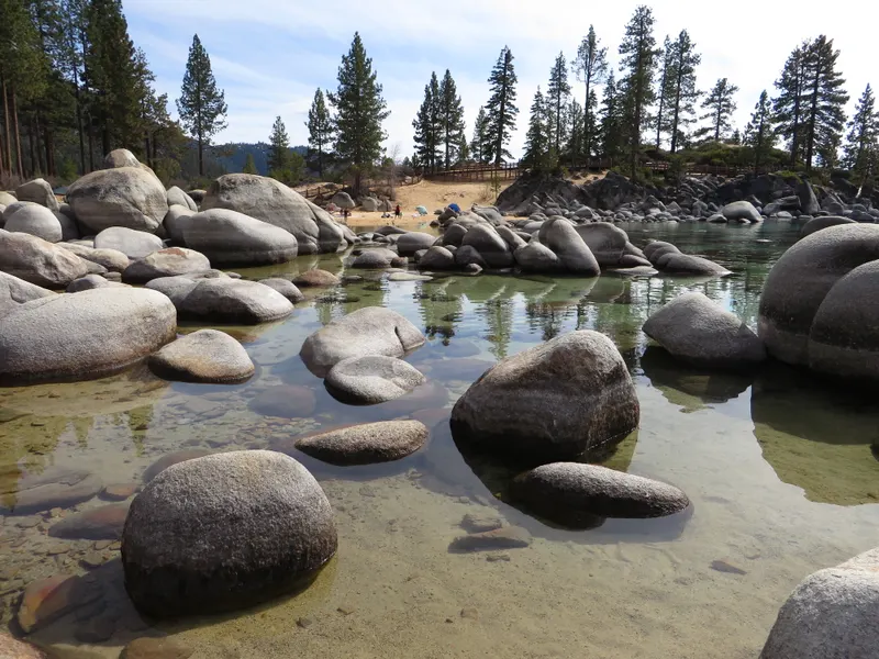 Turquoise water and a rocky shoreline at Sand Harbor with forested mountains across the lake.