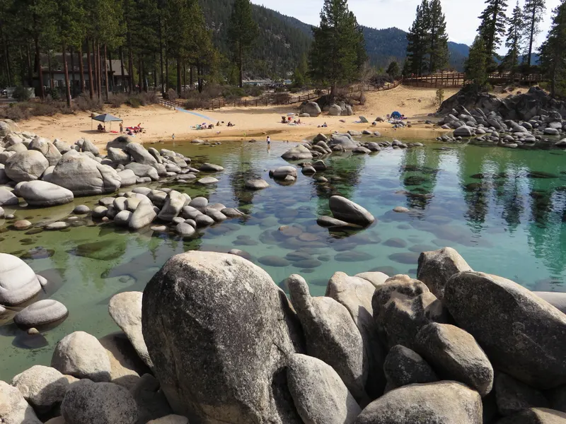 Granite boulders and a sandy cove at Sand Harbor with pines behind.