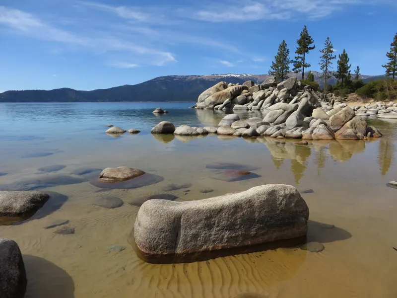 A rounded boulder in golden shallows at Sand Harbor, with a granite island, pines and the far shore behind.