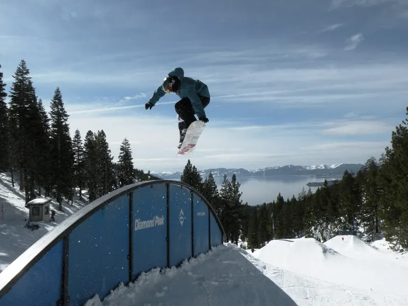 A snowboarder in the air over a rail at Diamond Peak, with Lake Tahoe in the distance.