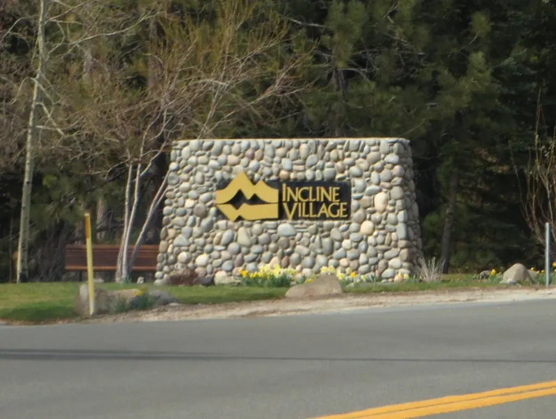 The stone Incline Village welcome sign beside the road, with spring flowers at its base.